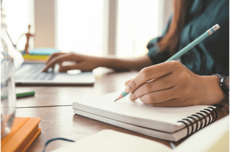 Picture of a person simultaneously writing in a notebook and typing on a laptop 